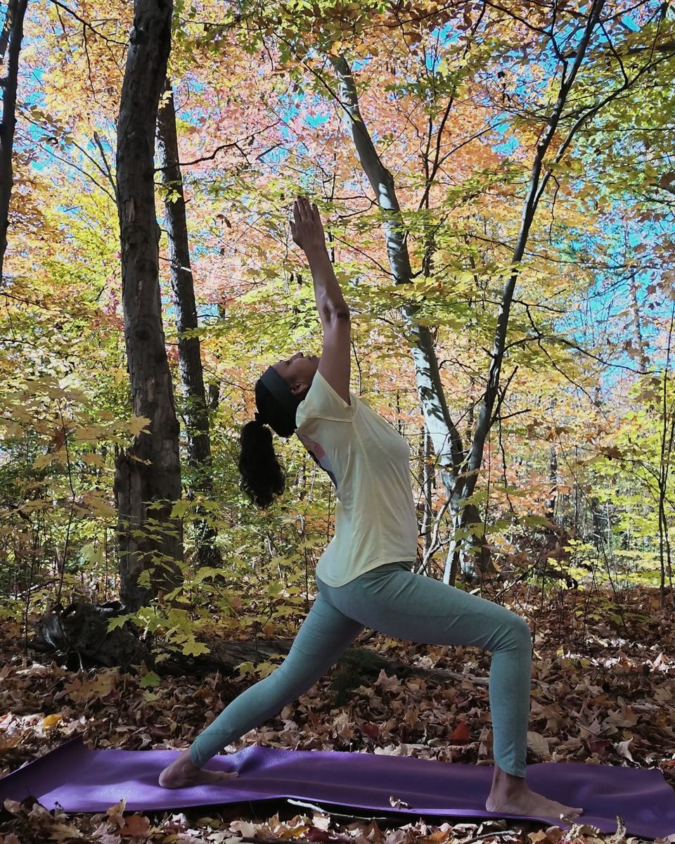 Sneh Lata holding a crescent lunge on a forest floor of maple leaves